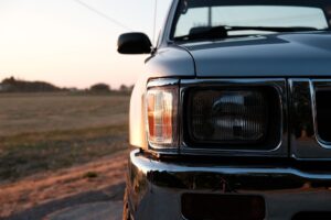Close-up of the front left headlight and side mirror of a black pickup truck, showcasing Custom Truck and SUV Builds in Metairie, parked outdoors at sunset with a field in the background.