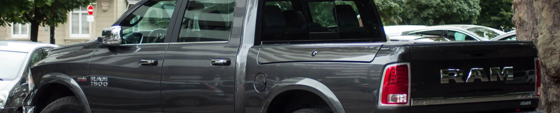 A gray RAM 1500 pickup truck, fresh from an engine tuneup, is parked on a street near trees and a building with balconies in the background.
